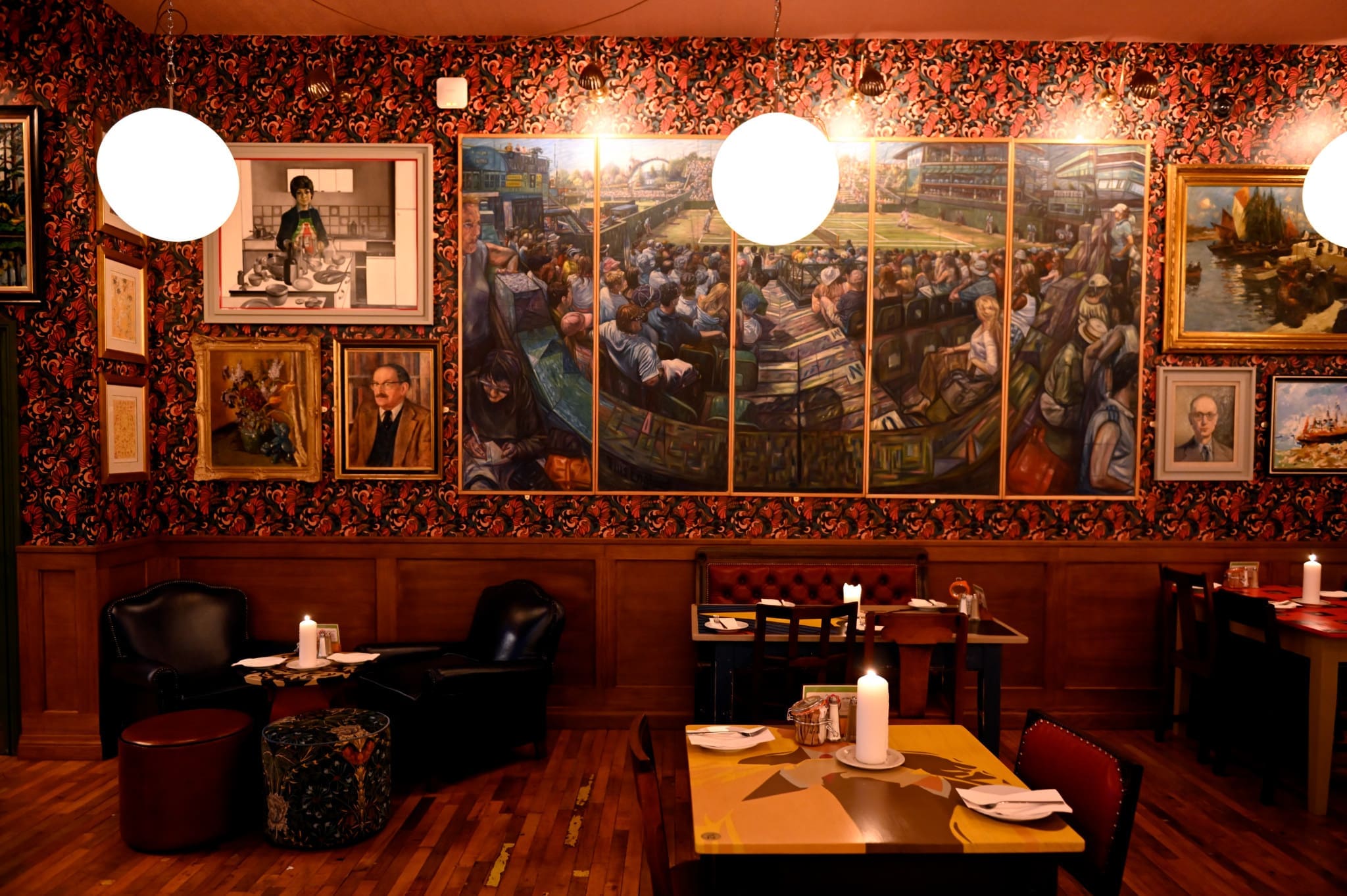 A cozy Porto restaurant interior with wooden floors, candlelit tables, and a wall covered in colorful, eclectic paintings and portraits under warm lighting from round hanging lamps.