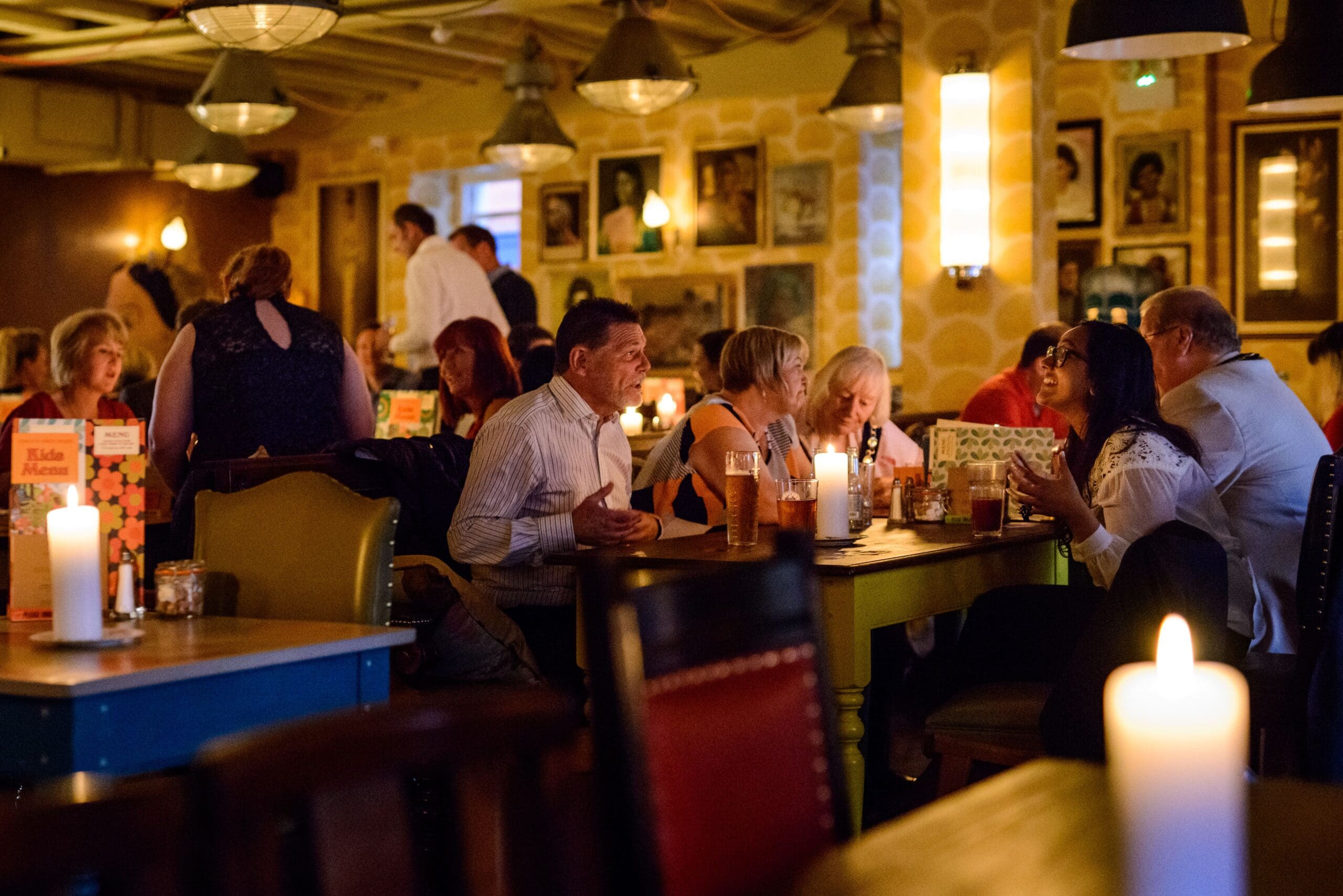 People sit at tables in a warmly lit restaurant or bar, talking and enjoying Corvo wines. Candles on the tables create a cozy atmosphere, while framed pictures decorate the walls and several groups of people socialize.