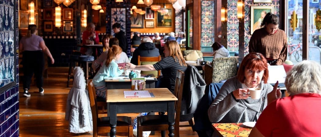 People sit at tables inside Bonito, a cozy, colorful café with patterned tiles, drinking, eating, and talking. Several artworks decorate the walls, and warm lighting gives the space a welcoming atmosphere.