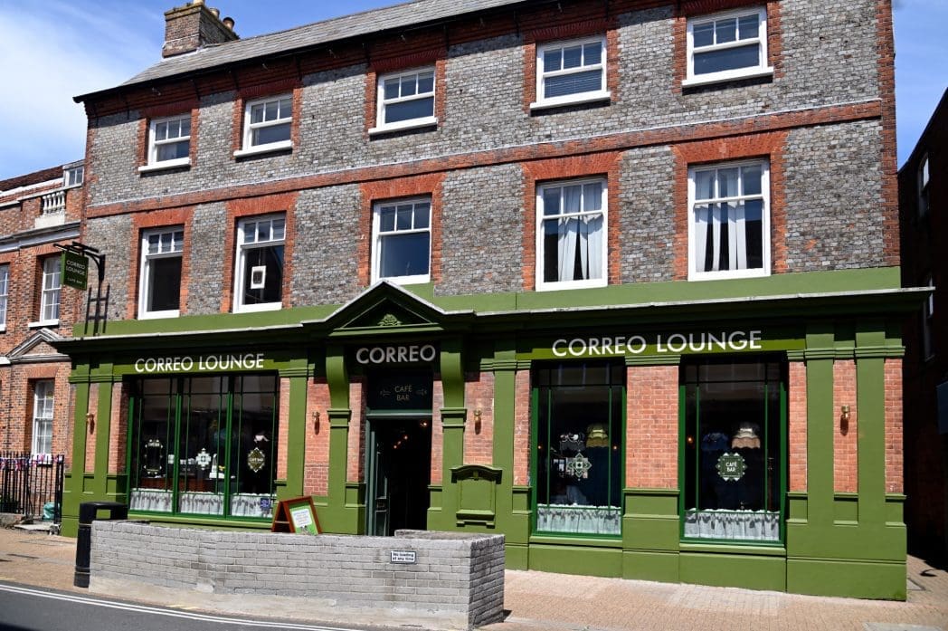 A three-story brick building with "CORREO LOUNGE" above the green-painted ground-floor café windows and entrance, the Correo stands proudly on a bustling street corner.