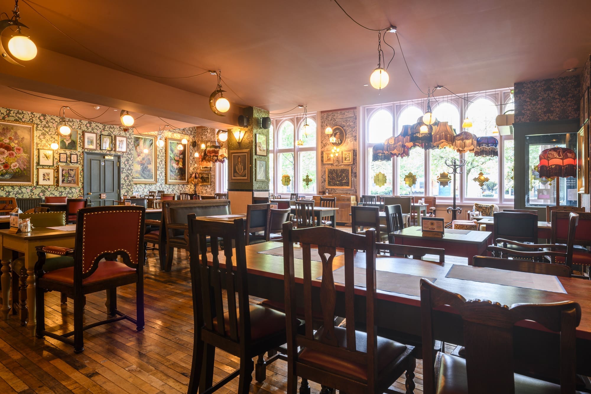 A cozy restaurant with eclectic vintage décor, Navio features wooden tables and mismatched chairs, floral wallpaper, framed art, hanging lamps, and large windows letting in natural light.